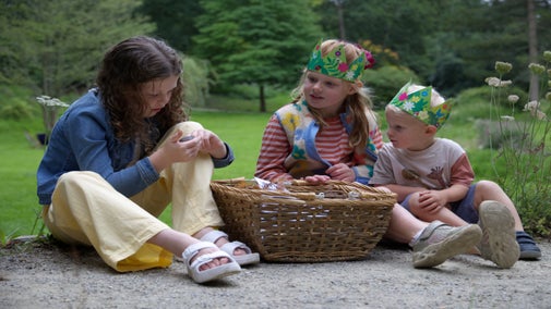 Three children sit making pictures with natural materials,